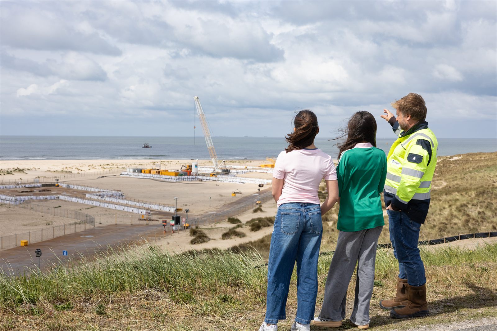 Medewerker en kinderen kijken uit over de bouwplaats en zee bij de Maasvlakte